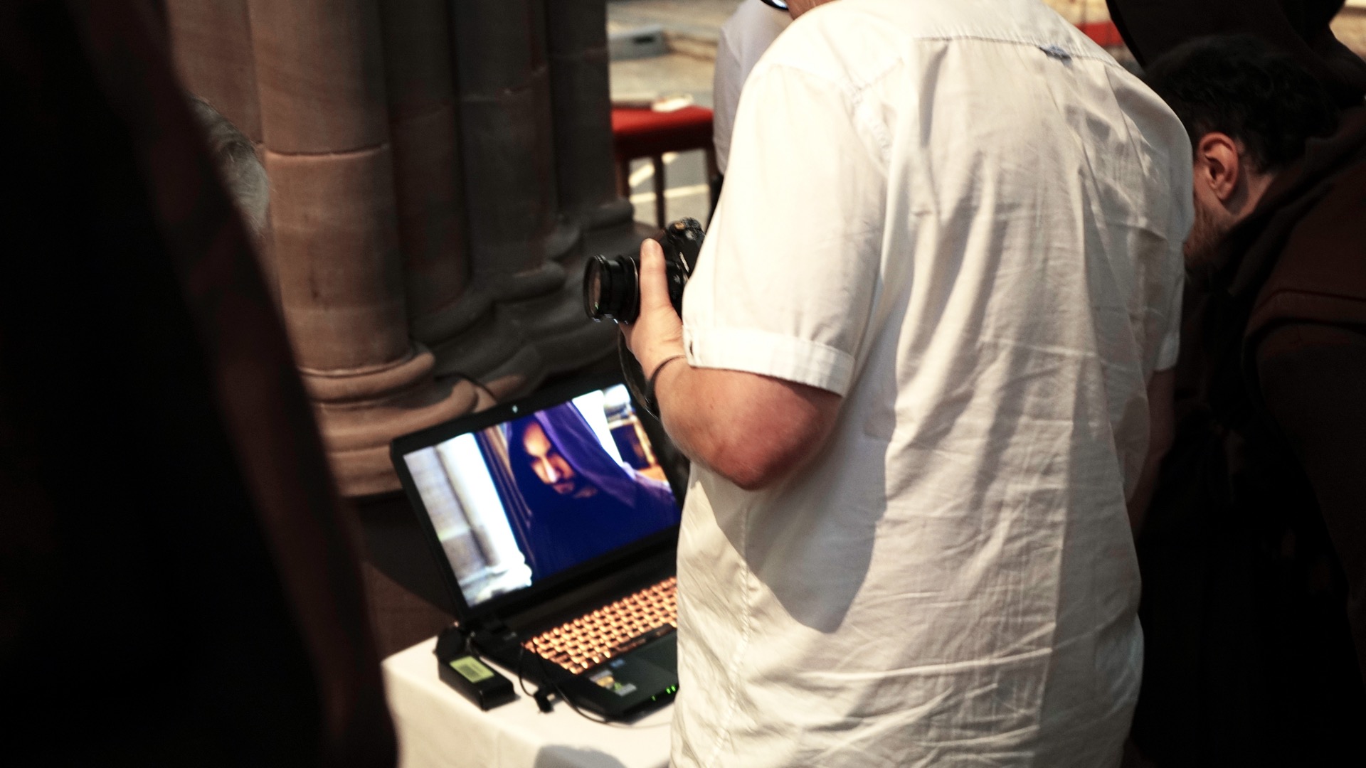 People looking at a computer screen that shows a close up of a cloaked monk.